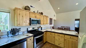 Kitchen with appliances with stainless steel finishes, light brown cabinetry, kitchen peninsula, and high vaulted ceiling