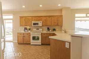 Kitchen with sink, white appliances, kitchen peninsula, and light tile patterned flooring