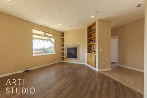 Unfurnished living room with built in shelves, dark lvp style floors, and a tiled fireplace