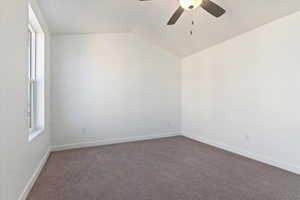 Empty room featuring dark colored carpet, vaulted ceiling, and ceiling fan