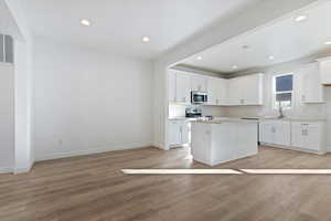 Kitchen with appliances with stainless steel finishes, white cabinetry, tasteful backsplash, light hardwood / wood-style floors, and a kitchen island