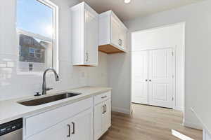 Kitchen with white cabinetry, dishwasher, sink, decorative backsplash, and light wood-type flooring