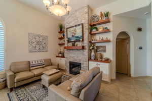 Living room with light tile patterned floors, a stone fireplace, and a chandelier