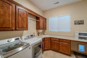 Clothes washing area with light tile patterned flooring, cabinets, washer and clothes dryer, and sink