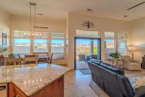 Kitchen with pendant lighting, light tile patterned floors, an inviting chandelier, a high ceiling, and light stone counters