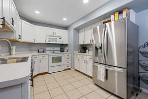 Kitchen with light tile patterned flooring, sink, white cabinets, and white appliances