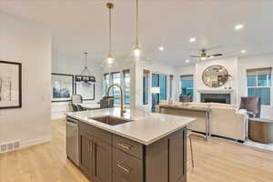 Kitchen featuring sink, light stone countertops, a center island with sink, decorative light fixtures, and stainless steel dishwasher