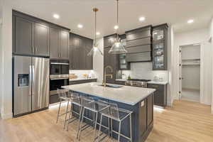 Kitchen with decorative light fixtures, sink, light stone counters, stainless steel appliances, and a center island with sink