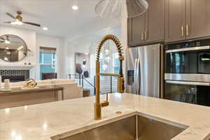 Kitchen with gray cabinetry, a tiled fireplace, ceiling fan, stainless steel appliances, and light stone countertops