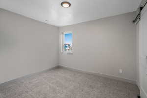 Carpeted empty room with a barn door and a textured ceiling