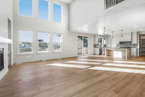 Unfurnished living room with light wood-type flooring, an inviting chandelier, and a towering ceiling