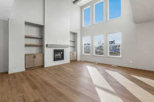 Unfurnished living room with built in shelves, a high ceiling, and light wood-type flooring