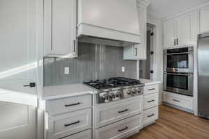 Kitchen with hardwood / wood-style floors, stainless steel appliances, tasteful backsplash, white cabinets, and custom exhaust hood