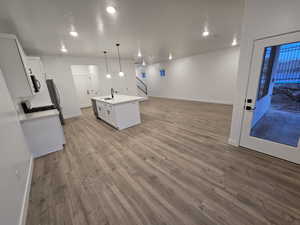 Kitchen with sink, white cabinets, hanging light fixtures, a kitchen island with sink, and light hardwood / wood-style flooring