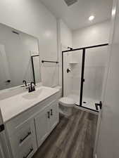 Bathroom with a shower with door, vanity, hardwood / wood-style floors, and toilet