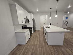 Kitchen featuring sink, a kitchen island with sink, stainless steel appliances, white cabinets, and decorative light fixtures