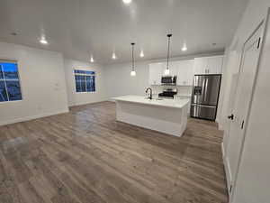 Kitchen featuring pendant lighting, sink, white cabinetry, stainless steel appliances, and a center island with sink