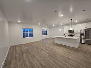 Kitchen with sink, white cabinetry, decorative light fixtures, an island with sink, and stainless steel appliances