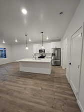 Kitchen with pendant lighting, appliances with stainless steel finishes, white cabinetry, dark hardwood / wood-style floors, and an island with sink