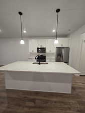 Kitchen with an island with sink, appliances with stainless steel finishes, pendant lighting, and white cabinets