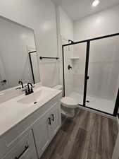 Bathroom with an enclosed shower, vanity, hardwood / wood-style flooring, and toilet