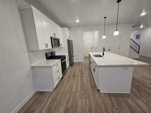 Kitchen with an island with sink, sink, white cabinets, hanging light fixtures, and stainless steel appliances