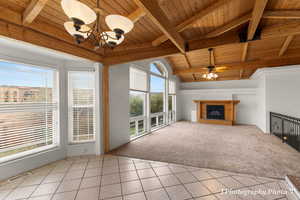 Unfurnished living room with vaulted ceiling with beams, wood ceiling, a brick fireplace, light colored carpet, and ceiling fan with notable chandelier