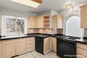 Kitchen featuring backsplash, light brown cabinetry, sink, and black appliances