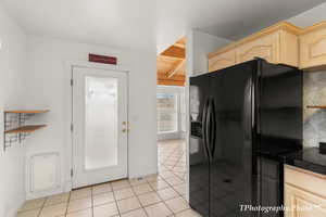 Kitchen featuring light tile patterned floors, wood ceiling, light brown cabinetry, black refrigerator with ice dispenser, and beamed ceiling