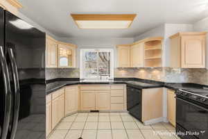 Kitchen with sink, light brown cabinets, light tile patterned floors, and black appliances