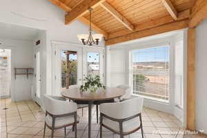 Tiled dining space with an inviting chandelier, vaulted ceiling with beams, and wooden ceiling