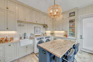 Laundry area with an inviting chandelier, cabinets, island seating, washer and dryer, and sink.