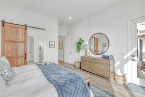 Bedroom with connected bathroom, a barn door, and light hardwood floors