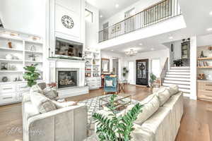 Living room with a notable chandelier, built-in features, light hardwood floors, and a high ceiling