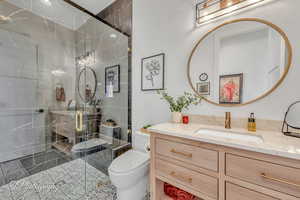 Bathroom featuring vanity, a shower with shower door, and toilet; adjacent to 2nd bedroom