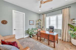 Bedroom set up as an office space with light hardwood flooring and double doors to courtyard