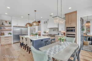 Kitchen with premium range hood, white & natural wood cabinetry, stainless steel appliances, a kitchen island, and decorative light fixtures