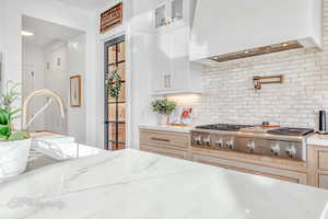 Kitchen featuring premium range hood, stainless steel gas stovetop, backsplash, light stone countertops, and light natural cabinets