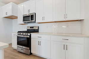 Kitchen featuring tasteful backsplash, light hardwood / wood-style flooring, white cabinets, and appliances with stainless steel finishes