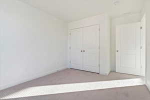 Unfurnished bedroom featuring light carpet and a closet