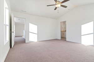 Unfurnished bedroom featuring ceiling fan, light colored carpet, high vaulted ceiling, and ensuite bath