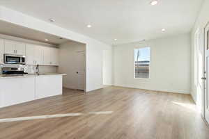 Kitchen featuring decorative backsplash, stainless steel appliances, white cabinets, and light wood-type flooring