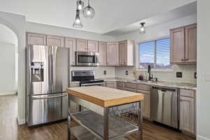 Kitchen featuring sink, stainless steel appliances, light stone countertops, decorative light fixtures, and light brown cabinets