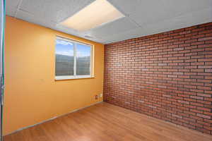 Spare room featuring a drop ceiling, hardwood / wood-style flooring, and brick wall