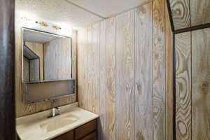 Bathroom featuring vanity, wooden walls, and a textured ceiling