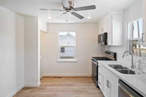 Kitchen featuring sink, tasteful backsplash, light wood-type flooring, appliances with stainless steel finishes, and white cabinets