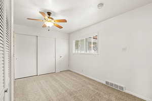 Primary bedroom with two closets, light carpet, and ceiling fan