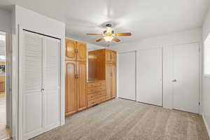 Primary bedroom with light carpet, two closets, and ceiling fan