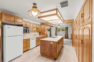 Kitchen featuring sink, light wood-type flooring, hanging light fixtures, a center island, and white appliances