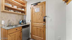 Kitchen with light stone counters, sink, decorative backsplash, and dishwasher